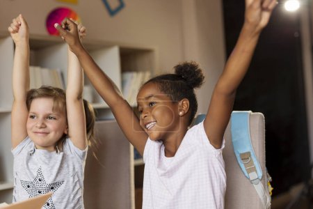 Foto de Dos niñas terminaron sus deberes y estudiaron para la escuela, celebrando, levantando las manos en el aire - Imagen libre de derechos