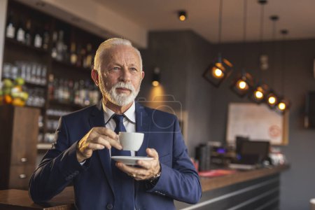 Foto de Retrato de un hombre de negocios mayor parado al lado de un mostrador de restaurante, tomando una taza de café - Imagen libre de derechos