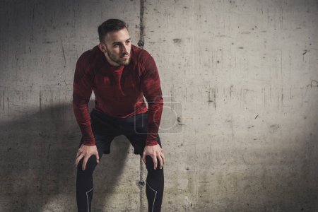 Téléchargez les photos : Homme sportif musclé portant des vêtements de sport, faisant une pause d'entraînement, debout et appuyé sur un mur en béton, coûteux - en image libre de droit