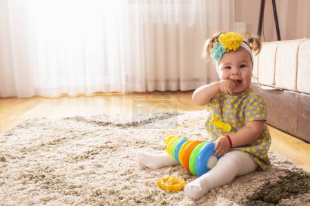 Photo for Beautiful little baby girl playing with colorful stack of different sized circles didactic toy and chewing her hands - Royalty Free Image