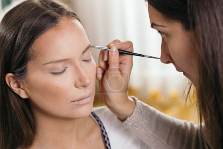 Photo for Make up artist working in a make up studio, applying the eyebrow shadows to female client's eyebrows - Royalty Free Image