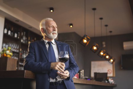 Téléchargez les photos : Homme d'affaires senior debout à côté d'un comptoir dans un restaurant, buvant du vin pendant une pause déjeuner - en image libre de droit