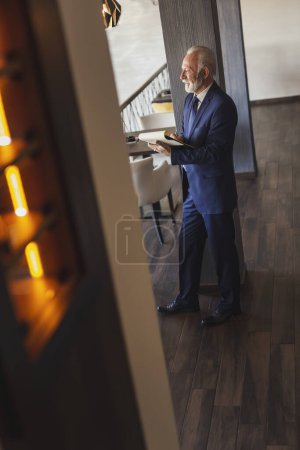 Photo for Senior businessman working in a modern office, taking notes in a planner, updating his schedule - Royalty Free Image