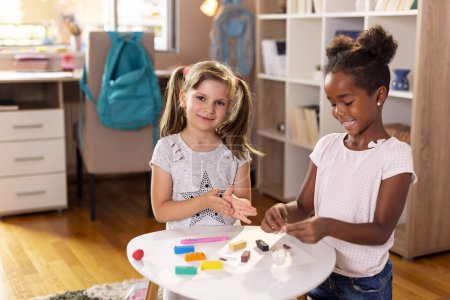 Foto de Dos niños en edad preescolar que juegan con plastilina colorida y se divierten. Concéntrate en la chica de la izquierda - Imagen libre de derechos