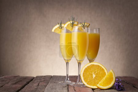 Foto de Cócteles Mimosa en copas de champán con zumo de naranja y vino espumoso decorado con hojas de lavanda y rodajas de naranja - Imagen libre de derechos