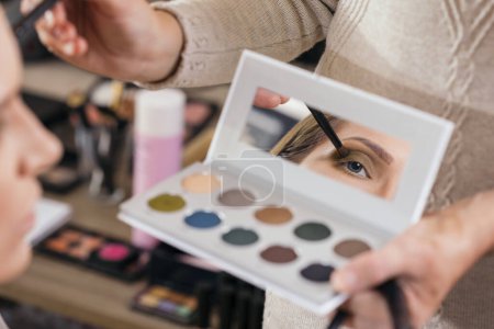 Téléchargez les photos : Maquilleuse travaillant dans un atelier de maquillage, ombrageant les paupières d'une cliente - en image libre de droit