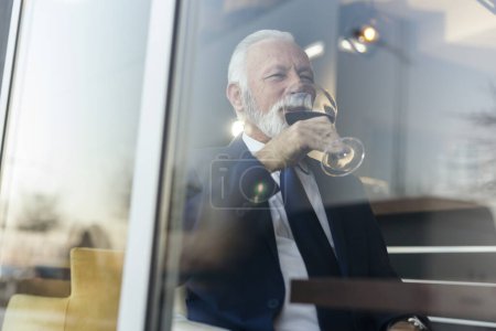 Foto de Retrato de un hombre de negocios mayor sentado en una mesa de restaurante, bebiendo vino - Imagen libre de derechos