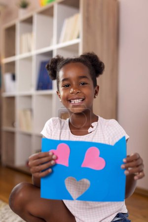 Téléchargez les photos : Belle petite fille tenant projet d'art fini pour l'école faite de papiers colorés - en image libre de droit