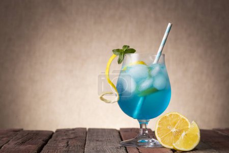 Foto de Cóctel laguna azul con licor de curazao azul, vodka, zumo de limón y refresco, decorado con rodajas de limón y hojas de menta en una mesa de madera rústica - Imagen libre de derechos