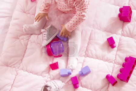 Téléchargez les photos : Vue grand angle de bébé fille portant une jupe tutu rose, assis sur une couette et jouant avec des blocs jouets - en image libre de droit