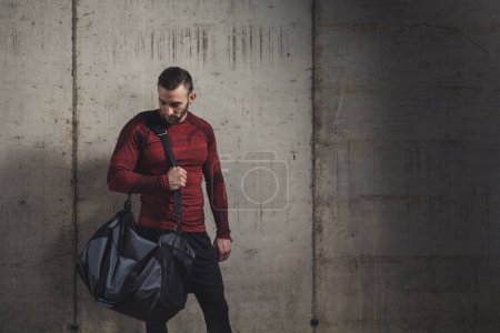 Photo for Muscular athetic man wearing sportswear and carrying a gym bag, going to a gym for a workout session - Royalty Free Image