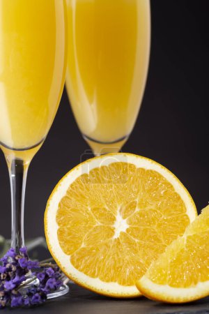 Photo for Detail of mimosa cocktails in champagne glasses with orange juice and sparkling wine decorated with lavender leaves and orange slices. Selective focus on the orange half - Royalty Free Image