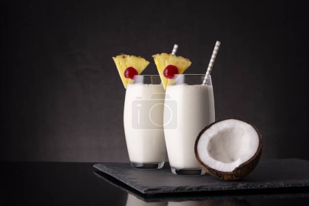 Téléchargez les photos : Deux verres de cocktail pina colada au rhum foncé, jus d'ananas et crème de coco, décorés de tranches d'ananas et de cerise marasquin et moitié noix de coco - en image libre de droit