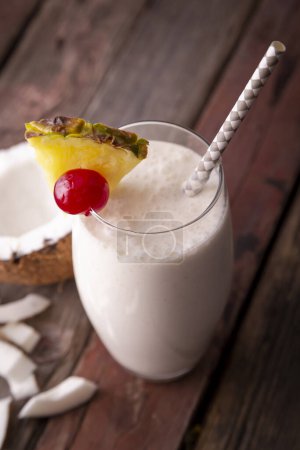 Photo for High angle view of a glass of pina colada cocktail with dark rum, pineapple juice and coconut cream, decorated with pineapple slices and maraschino cherry - Royalty Free Image
