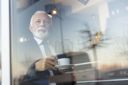 Téléchargez les photos : Homme d'affaires senior dans un bureau moderne travaillant sur un ordinateur portable et buvant du café - en image libre de droit