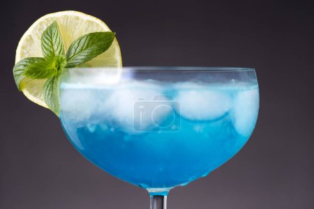 Foto de Detalle de cóctel laguna azul con licor de curazao azul, vodka, zumo de limón y refresco, decorado con rodajas de limón y hojas de menta - Imagen libre de derechos