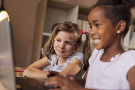 Téléchargez les photos : Deux petites filles ayant une classe en ligne utilisant un ordinateur portable appel vidéo, e-learning à la maison en raison de Covid 19 mesures de distanciation sociale pandémique ; enfants faisant des conférences virtuelles à domicile - en image libre de droit