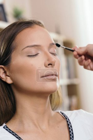 Foto de Maquillaje artista que trabaja en un estudio de maquillaje, aplicando las sombras de las cejas a las cejas del cliente femenino - Imagen libre de derechos