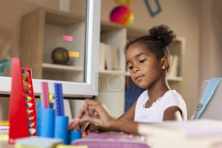 Photo for Beautiful little girl sitting at her desk, doing homework and preparing for a new shool day - Royalty Free Image