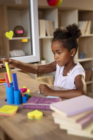 Photo for Beautiful little girl sitting at her desk, doing homework and preparing for a new shool day - Royalty Free Image