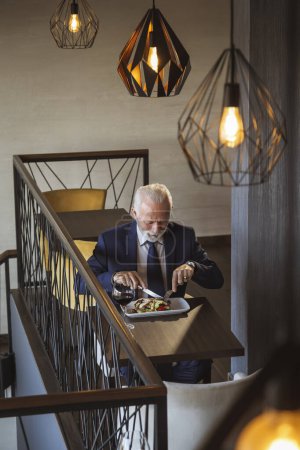 Photo for Senior businessman taking a lunch break, eating in a restaurant - Royalty Free Image