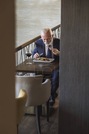 Photo for Senior businessman taking a lunch break, eating in a restaurant - Royalty Free Image