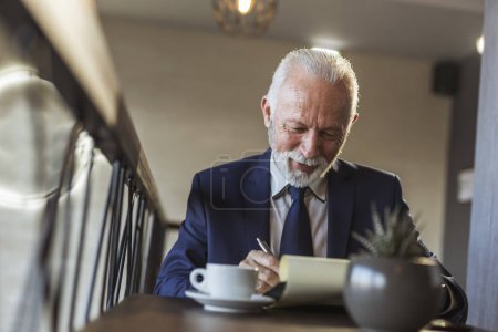 Foto de Hombre de negocios sénior sentado en un moderno restaurante edificio de oficinas, bebiendo café y firmando un nuevo contrato, satisfecho y feliz - Imagen libre de derechos
