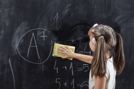 Photo for Schoolgirl wiping blackboard with a sponge after solving math problems and getting an A in math. Focus on the sponge and the hand - Royalty Free Image
