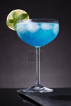 Foto de Cóctel laguna azul con licor de curazao azul, vodka, zumo de limón y refrescos, decorado con rodajas de limón y hojas de menta. Enfoque selectivo en las hojas de menta - Imagen libre de derechos