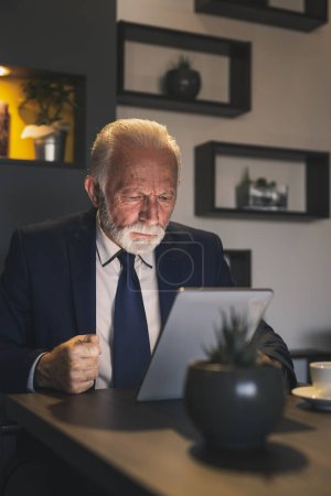 Téléchargez les photos : Homme d'affaires senior dans un restaurant, travaillant sur une tablette informatique, coûteux et sérieux - en image libre de droit