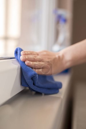 Photo for Detail of female hands wiping windows with a cleanser spray and a cloth; housekeeping assistant wiping windows - Royalty Free Image