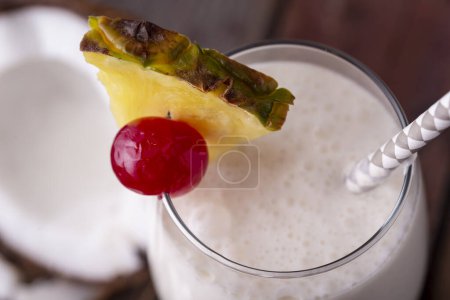 Photo for High angle view of a glass of pina colada cocktail with dark rum, pineapple juice and coconut cream, decorated with pineapple slices and maraschino cherry - Royalty Free Image