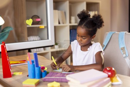 Téléchargez les photos : Belle petite fille assise à un bureau, dessinant avec des surligneurs sur des notes collantes colorées, se préparant pour le premier jour d'école - en image libre de droit