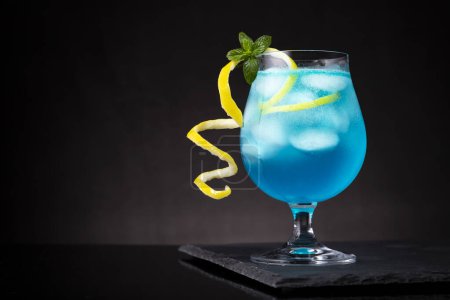 Téléchargez les photos : Cocktail lagon bleu avec liqueur de curaçao bleu, vodka, jus de citron et soda, décoré de tranches de citron et de feuilles de menthe. Focus sélectif sur les feuilles de menthe - en image libre de droit
