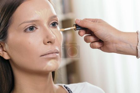 Photo for Make up artist applying liquid face powder foundation to a female client's face, contouring the face - Royalty Free Image