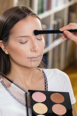 Téléchargez les photos : Maquilleuse travaillant dans un studio de maquillage, appliquant les surligneurs sur le visage de la cliente - en image libre de droit