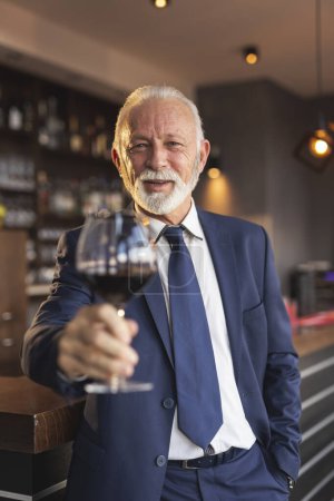 Photo for Senior businessman standing next to a counter in a restaurant, making a toast after making a successful business deal - Royalty Free Image