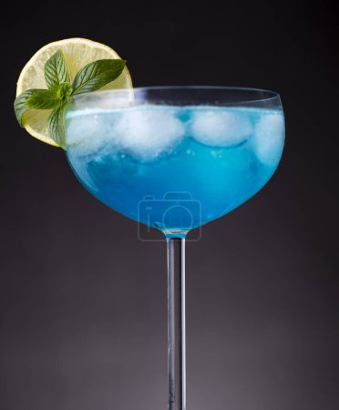 Téléchargez les photos : Détail du cocktail lagon bleu avec liqueur de curaçao bleu, vodka, jus de citron et soda, décoré de tranches de citron et de feuilles de menthe. Focus sélectif sur les feuilles de menthe - en image libre de droit