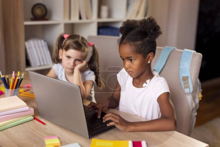 Foto de Dos niñas hermosas sentadas en un escritorio, haciendo deberes, terminando un proyecto para la escuela en una computadora portátil - Imagen libre de derechos