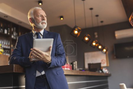 Téléchargez les photos : Gestionnaire de restaurant principal debout à côté d'un comptoir, à l'aide d'une tablette - en image libre de droit