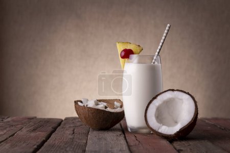 Photo for Glass of pina colada cocktail with dark rum, pineapple juice and coconut cream, decorated with pineapple slices and maraschino cherry on rustic wooden table - Royalty Free Image