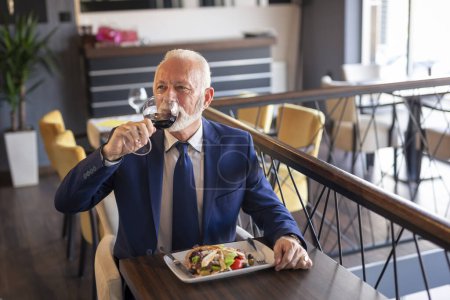 Téléchargez les photos : Homme d'affaires senior faisant une pause, buvant du vin et déjeunant au restaurant - en image libre de droit
