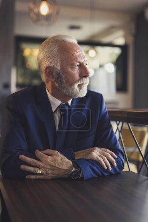 Photo for Portrait of a pensive senior businessman sitting in a modern office building restaurant, looking at the distance - Royalty Free Image