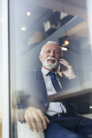 Senior-Geschäftsmann sitzt an einem Restauranttisch und telefoniert