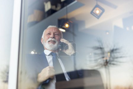 Téléchargez les photos : Homme d'affaires senior assis à une table de restaurant, ayant une conversation téléphonique - en image libre de droit