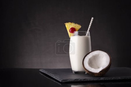 Photo for Glass of pina colada cocktail with dark rum, pineapple juice and coconut cream, decorated with pineapple slices, maraschino cherry and coconut half - Royalty Free Image