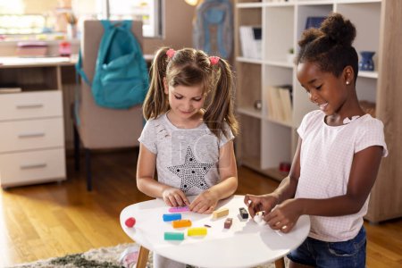 Foto de Dos niñas de la escuela jugando con la masa de juego de colores, haciendo un muñeco de nieve y una serpiente. Concéntrate en la chica de la izquierda - Imagen libre de derechos