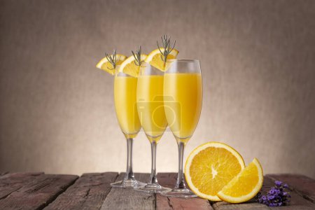 Foto de Cócteles Mimosa en copas de champán con zumo de naranja y vino espumoso decorado con hojas de lavanda y rodajas de naranja - Imagen libre de derechos