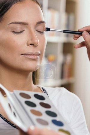 Téléchargez les photos : Maquilleuse travaillant dans un atelier de maquillage, ombrageant les paupières d'une cliente - en image libre de droit