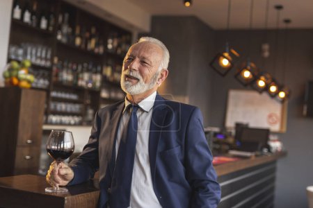 Téléchargez les photos : Homme d'affaires principal debout à côté d'un comptoir dans un restaurant, buvant du vin et ayant une conversation avec un collègue pendant une pause déjeuner - en image libre de droit
